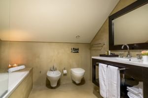 Modernes Badezimmer im Universal Boutique Hotel mit beigen Wänden, Badewanne, wandhängender Toilette und Bidet, dunklem Holzwaschtisch.