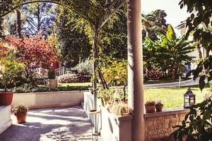 Überdachte Terrasse im Hotel Savoy Gardone mit Steinsäulen, Topfpflanzen und Blick auf den Landschaftsgarten mit buntem Herbstlaub.