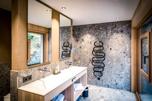 Salle de bain luxueuse avec murs en marbre, meuble-lavabo en bois, grand miroir, radiateurs sèche-serviettes noirs à l'hôtel Hauserei.