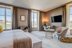Elegantes Doppelzimmer im Hotel Fleur de Loire Blois mit großem Bett, beigen Sesseln, Wandfernseher und französischen Fenstern mit Stadtblick.