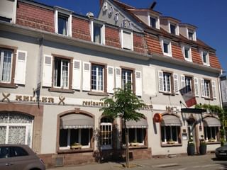 Bâtiment de trois étages de l'Hôtel Beauséjour à Colmar avec façade blanche, toit de tuiles rouges, volets traditionnels et restaurant au rez-de-chaussée.