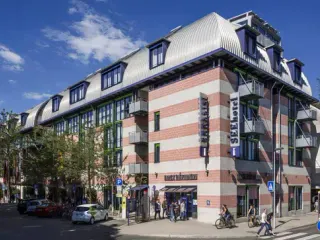 Modernes gestreiftes Gebäude des SEEhotel Friedrichshafen mit rot-weißer Fassade, Mansardendach und Balkonen an einem sonnigen Tag.