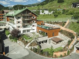 Vue aérienne de l'hôtel Schwarzer Adler à St. Anton avec architecture alpine traditionnelle, extension spa moderne et terrasse.