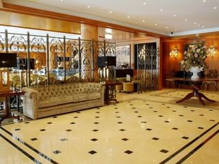 Luxuriöse Lobby des Hotel Moliceiro Aveiro mit Marmorböden, verzierten Eisengeländern, beigem Chesterfield-Sofa und Blumenarrangement.