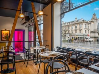Modernes Bar-Interieur mit schwarzen Bistrostühlen, runden Tischen, sichtbaren Holzbalken und bodentiefen Fenstern mit Blick auf eine Straße in Tours.