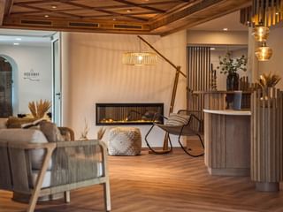 Moderne Hotelrezeption im Bergrose Strobl mit Holzrezeption, zeitgemäßem Sitzbereich, Kamin und warmer Beleuchtung.