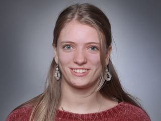 Portrait professionnel d'Elisa Simonazzi aux cheveux blonds longs, portant des boucles d'oreilles décoratives et un pull rouge.