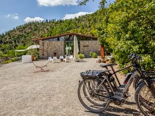 Steingebäude mit Terrasse und weißen Sonnenliegen im Agriturismo Le Valli in Casciana Terme. Fahrräder auf Kiesplatz, Hügel im Hintergrund.