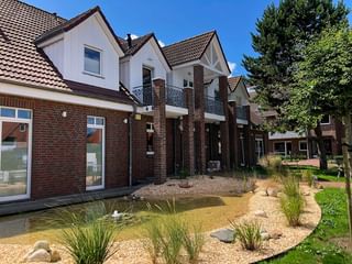 Modernes Hotel Upstalsboom Gebäude mit weißen Wänden, roten Ziegeldächern, Backsteinsäulen und Balkonen. Angelegter Garten mit Teich im Vordergrund.