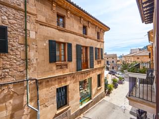 Bâtiment traditionnel en grès à Pollenca avec volets verts et toit de tuiles, donnant sur une rue calme à l'architecture méditerranéenne.