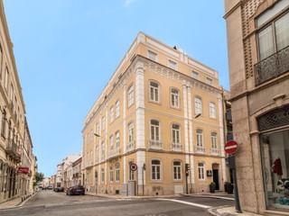 Gelbes Eckgebäude des Universal Boutique Hotels mit weißen Verzierungen und Balkonen an einer Kopfsteinpflasterstraße in Figueira da Foz.