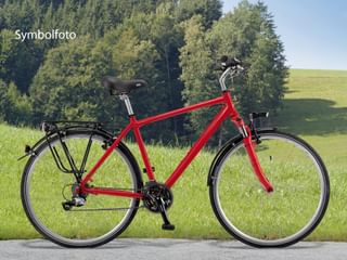 Rotes Tourenrad mit 21 Gängen, schwarzem Sattel, Gepäckträger und Ständer am Straßenrand. Grüne Wiese und Wald im Hintergrund.