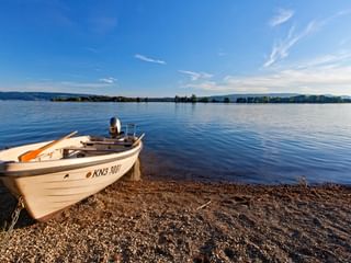 Weißes Ruderboot mit Kennzeichen KN3-001 am Kieselstrand des Bodensees unter blauem Himmel mit dünnen Wolken.
