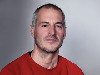 Porträt von Pablo Bachiller in einem roten Shirt vor hellgrauem Hintergrund. Er hat kurzes graues Haar und einen Bart.