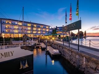 Bad Horn Hotel und Spa beleuchtet in der Dämmerung am Bodenseeufer mit Hafen, Flaggen und Boot namens Emily im Vordergrund.