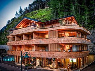 Bâtiment d'hôtel moderne incurvé avec façade en bois et éclairage chaleureux, niché contre une colline boisée dans les Alpes autrichiennes.