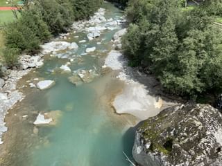 Luftaufnahme des Rheins mit türkisfarbenem Wasser, das durch ein steiniges Flussbett mit großen weißen Steinen und Felsbrocken fließt.