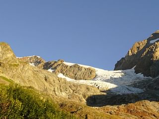 Panoramablick auf das Mont-Blanc-Massiv mit schneebedeckten Gipfeln, Gletschern und grünen Almwiesen mit Wildblumen im Vordergrund.