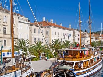Traditionelle Holzboote im Hafen von Mali Lošinj, Kroatien. Historische weiße Gebäude mit roten Dächern säumen die Uferpromenade.