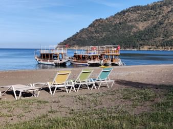 Drei Liegestühle stehen am Strand und im Meer befinden sich drei Holzboote