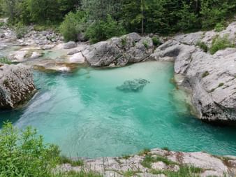 Türkisfarbener Fluss, breitere Stelle umgeben von geschiffenen Steinen und Bäumen.
