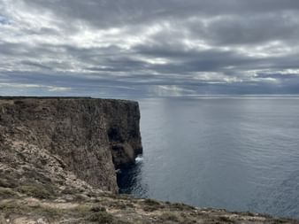 Steile Felsklippen am Cabo de São Vicente, die unter dramatischem Wolkenhimmel in den Atlantik abfallen, in der Algarve.