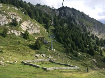 Seilbahn, die durch die Landschaft führt, über den mauerhohen Überresten eines alten Steinhauses.