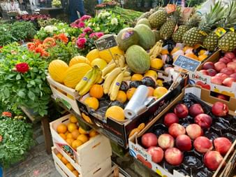 Bunte Früchteauslage auf dem Markt in Kopenhagen mit Melonen, Ananas, Bananen, Orangen und Pfirsichen in Holzkisten mit Preisschildern.