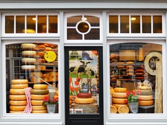 Devanture d'une fromagerie à Gouda avec de grandes vitrines exposant des piles de meules de fromage jaune et des décorations hollandaises.