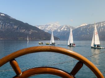 Vue depuis Spiez sur le lac de Thoune avec voiliers sur l'eau calme, montagnes enneigées en arrière-plan et balustrade orange au premier plan.