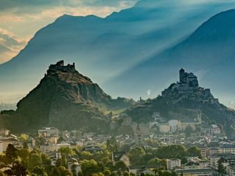 Two mountain peaks with an old and an intact castle. Down in the valley is Sion.