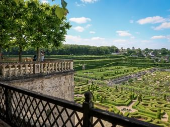 Jardins à la française du Château de Villandry avec haies géométriques et motifs ornementaux. Balustrade en pierre au premier plan, village visible.
