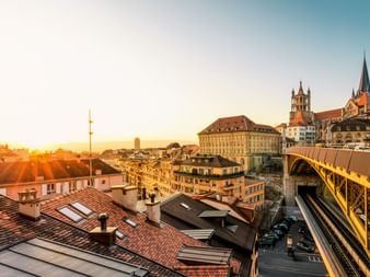 Sonnenuntergang über Lausannes Dächern mit Kathedralentürmen und gelber Brücke. Goldenes Licht beleuchtet die historischen Gebäude.