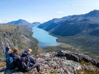 Drei Wanderer sitzen bei Gjendetunga in Norwegen und schauen auf den See, der unter ihnen liegt.