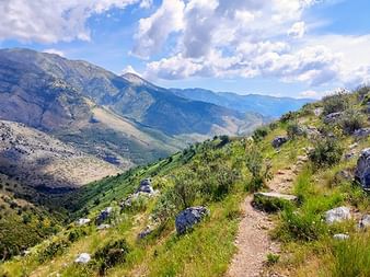 Spektakulärer Balkan-Bergwanderweg Ausblick Gewundener Wanderweg durch felsiges Gelände im Balkan mit spektakulärem Blick auf Bergtal unter bewölktem blauen Himmel.
