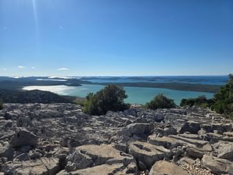 Panoramablick auf den Vransko-See in Kroatien von einem felsigen Hügel. Der türkisfarbene See erstreckt sich bis zum Horizont mit Bergen.