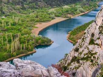 Luftaufnahme des Cetina-Flusses, der sich durch eine Schlucht in Kroatien schlängelt, umgeben von Felsklippen und üppiger grüner Vegetation.