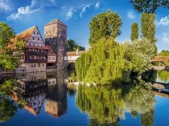 Fachwerkhäuser und mittelalterlicher Turm spiegeln sich in der Pegnitz in Nürnbergs Altstadt, mit Steinbrücke und Trauerweiden.
