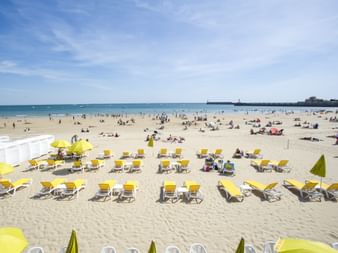 Plage animée de la côte atlantique avec des rangées de transats jaunes au premier plan et de nombreux baigneurs sur le sable doré.