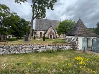 Kirche aus Steinen umgeben von Wiese und Laubbäumen