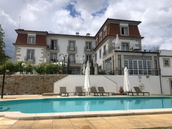 Weißes Herrenhaus-Hotel mit rotem Ziegeldach und Swimmingpool. Pousada de São Romão verfügt über mehrere Balkone und eine Terrasse mit Poolblick.