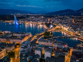 Genf von oben bei Nacht. Man sieht den See und die Stadt beleuchtet.