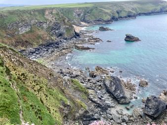 Zerklüftete Küste Cornwalls mit dunklen Felsformationen, türkisfarbenem Wasser und grünen Klippen. Kleine Buchten und Felsvorsprünge säumen die Küste.