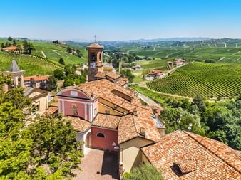 Vue aérienne d'un village italien historique au Piémont avec toits de tuiles rouges, clocher et église entourés de collines viticoles.