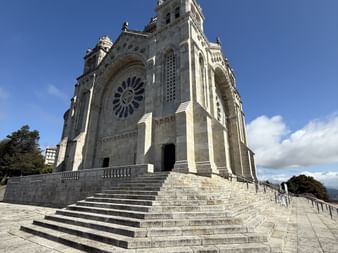 Steinkirche auf Monte Santa Luzia mit verzierter Fassade, Rosettenfenster und Zwillingstürmen. Breite Steintreppe führt zum Eingang unter blauem Himmel.