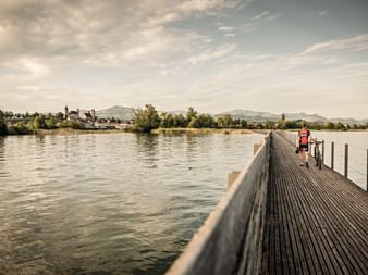 Un homme traverse un pont en bois qui mène à la vieille ville de Rapperswil. La route du cœur. Vacances à vélo avec Eurotrek.