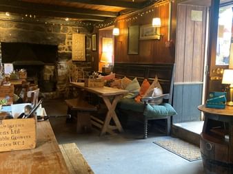 Gemütliches Pub-Interieur in Cornwall mit sichtbaren Holzbalken, Steinkamin, Lichterketten, Holzmöbeln und bunten Kissen auf Bänken.