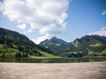 Lac de Schwarzsee avec eau calme reflétant les montagnes alpines vertes et forêts sous un ciel bleu avec nuages blancs dans la région de Fribourg.