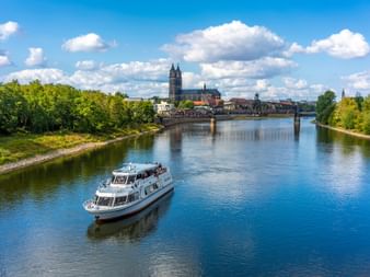Weißes Passagierboot auf der Elbe in Magdeburg mit gotischem Dom und historischer Brücke im Hintergrund unter blauem Himmel.