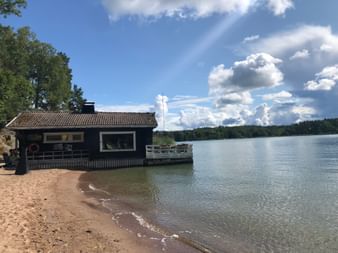 Ein kleines Haus am Meer in Finnland mit Sand und Bäumen.